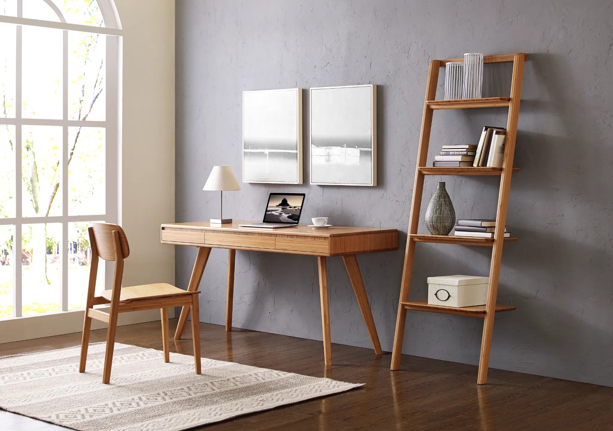 A renewable Currant Bamboo Writing Desk by Greenington in caramel color, placed in an office room with a side bookshelf and a chair.